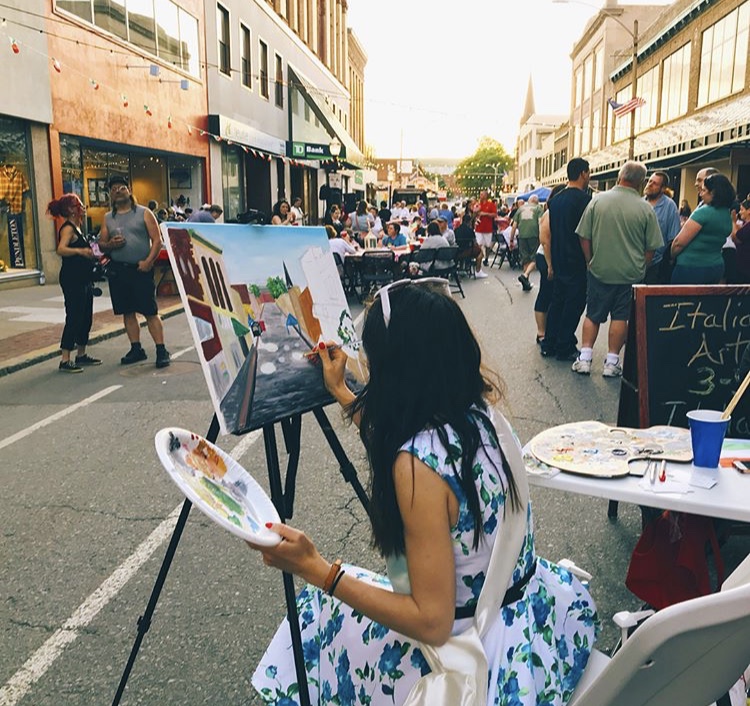 Woman painting on a canvas in the middle of a busy street.